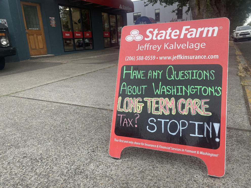 A red State Farm sandwich board with a chalk message, "Have any questions about Washington's Long Term Care Tax? STOP IN"