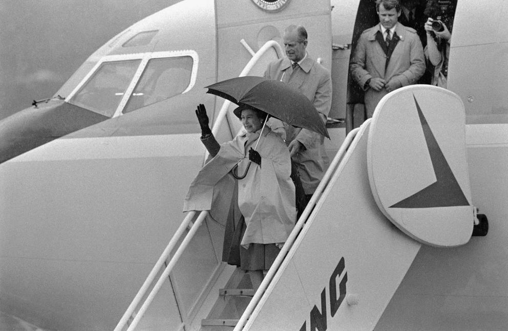 Queen Elizabeth exits an airplane holding an umbrella