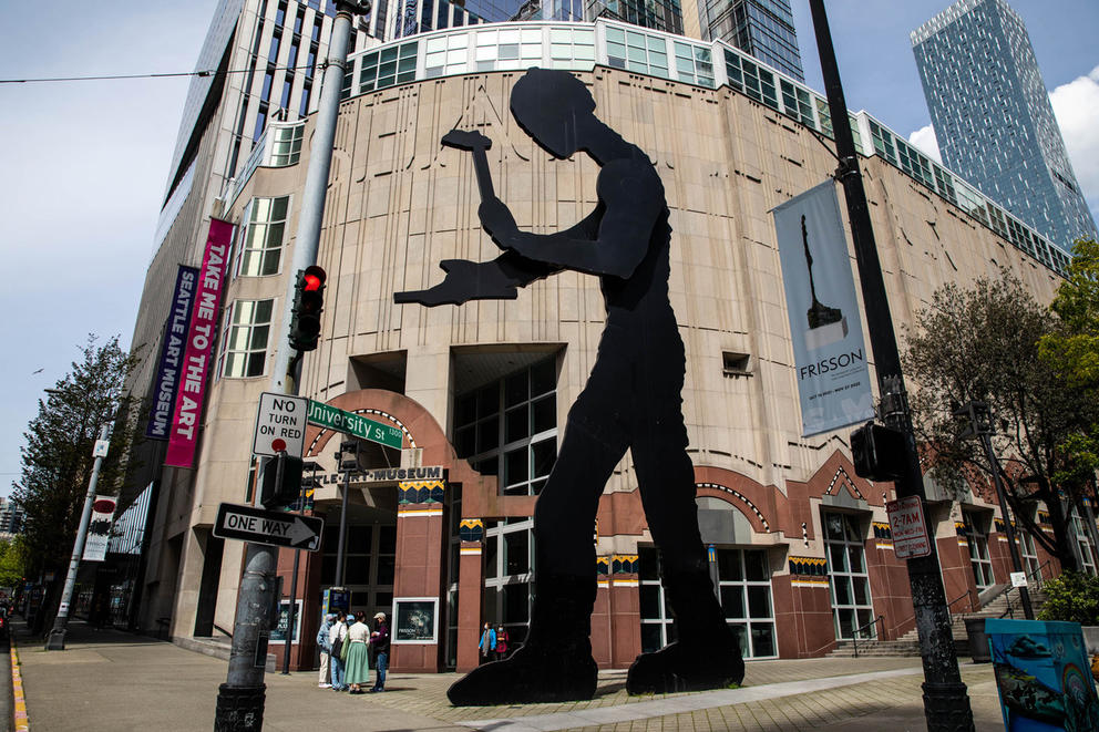 Large flat, black sculpture of a worker in front of the postmodern facade of the Seattle Art Museum
