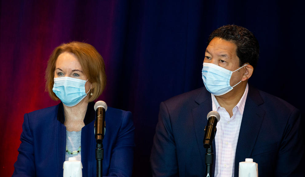 former mayor jenny durkan stands next to current mayor bruce harrell both wearing blue surgical masks