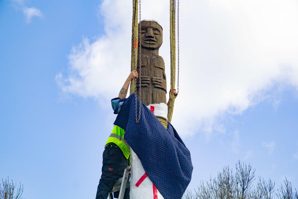 Carved wooden pole with worker to the left unveiling it 