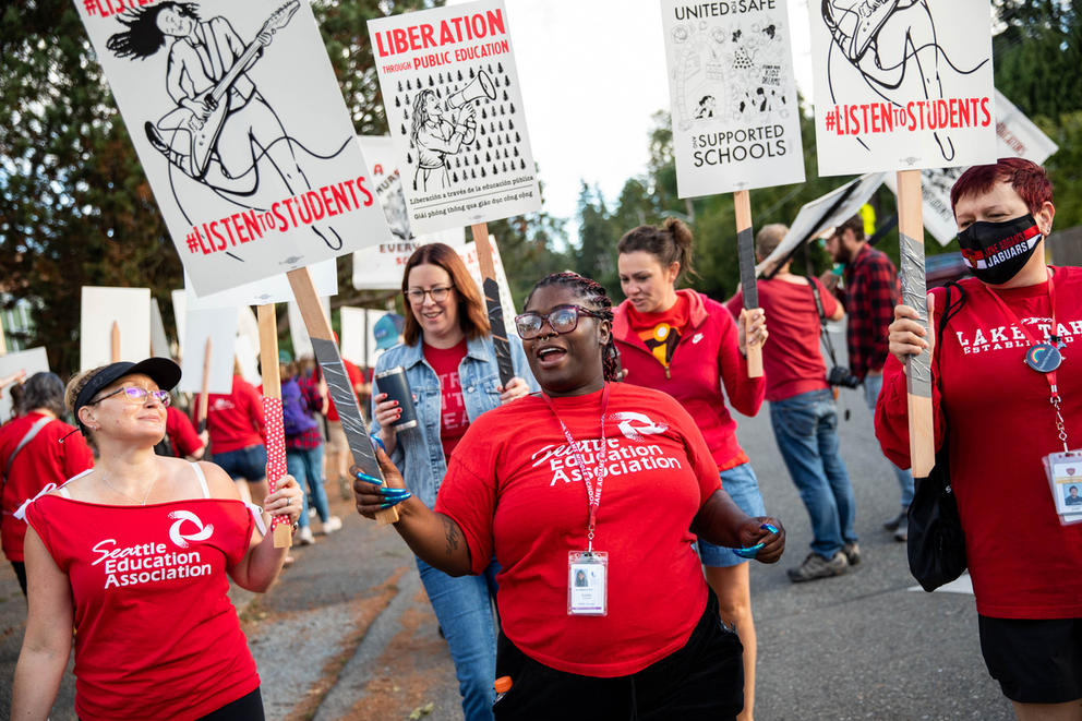 Teachers wearing red march on a street holding signs.