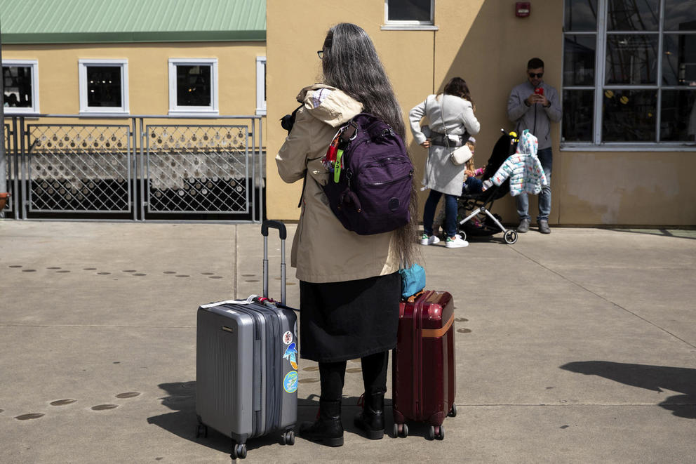 A woman faces away from the camera, suitcases beside her