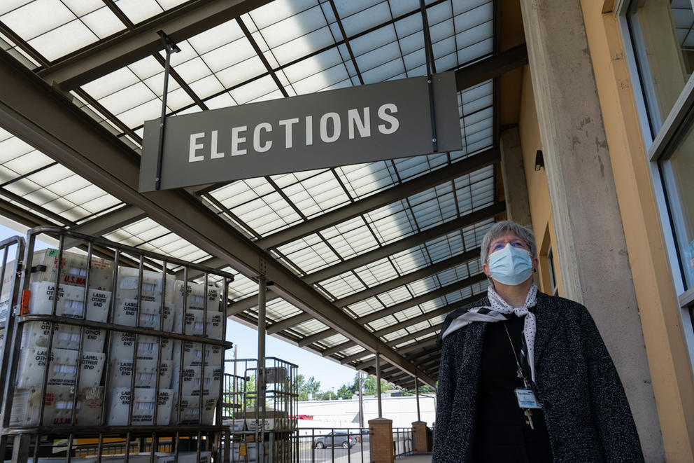 A woman wearing a face mask walks beneath a sign that reads "Elections"