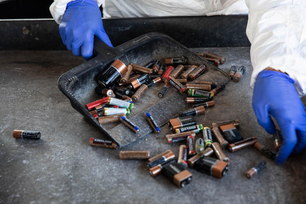a person's hands in blue latex gloves are shown pushing batteries into a dust bin 
