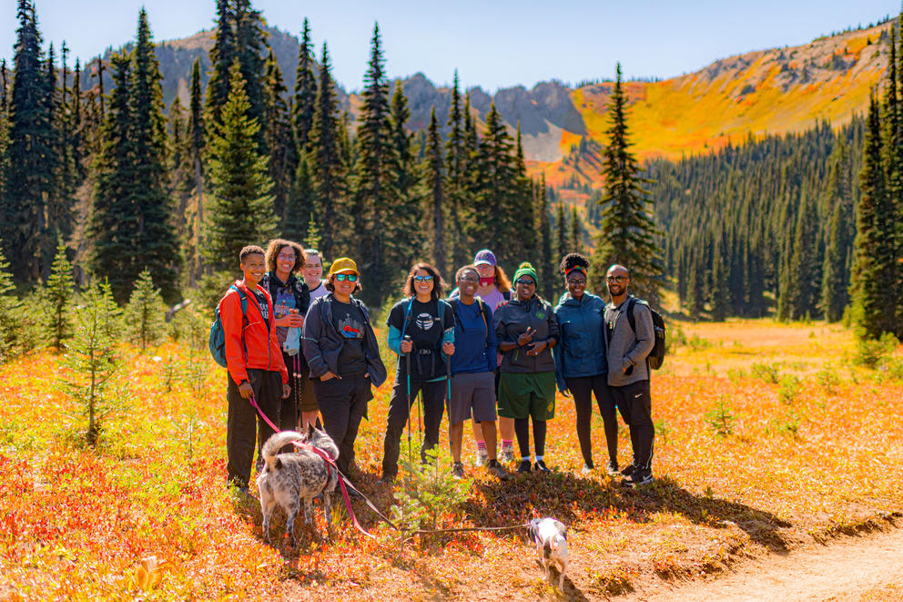 A group of 10 hikers and two dogs pose for a photo in front of trees