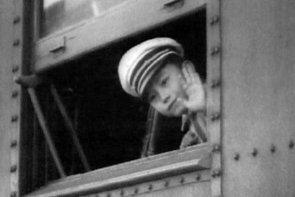 A Japanese American bot is seen waving from a train window. 