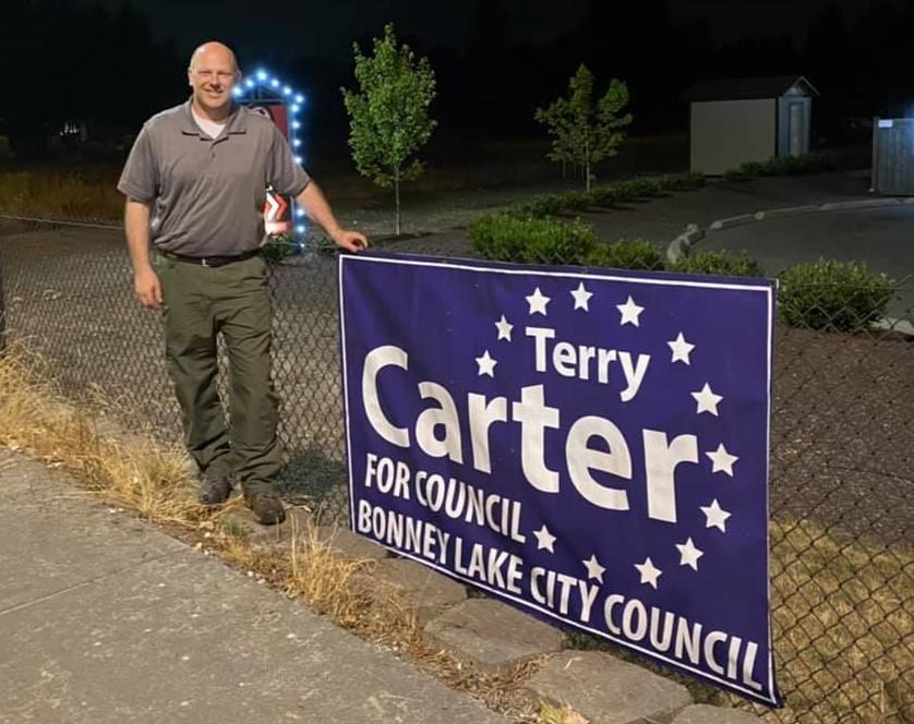 Terry Carter puts his hand on top of a blue and white campaign sign for his re-election campaign