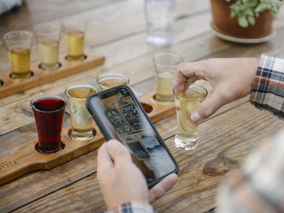 someone holding a phone above a table near a flight of ciders 