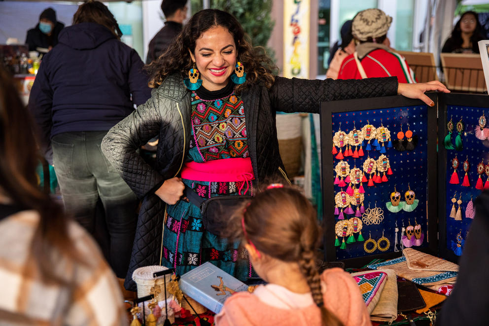 A woman smiles down at a girl from behind a table lined with jewelry for sale