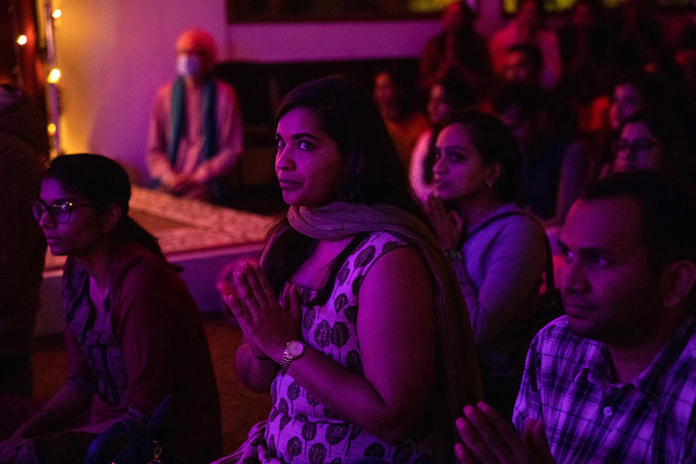 A group of people press their hands together in prayer in red and purple light