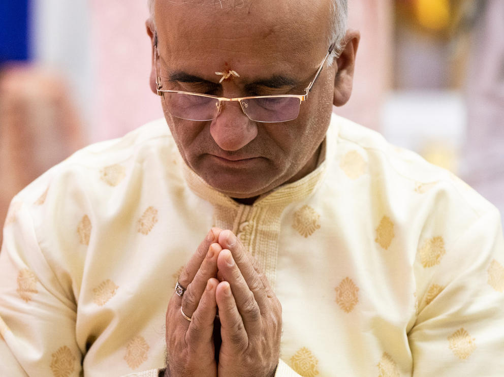 A close up shot with a man with his hands pressed together and head bowed in prayer