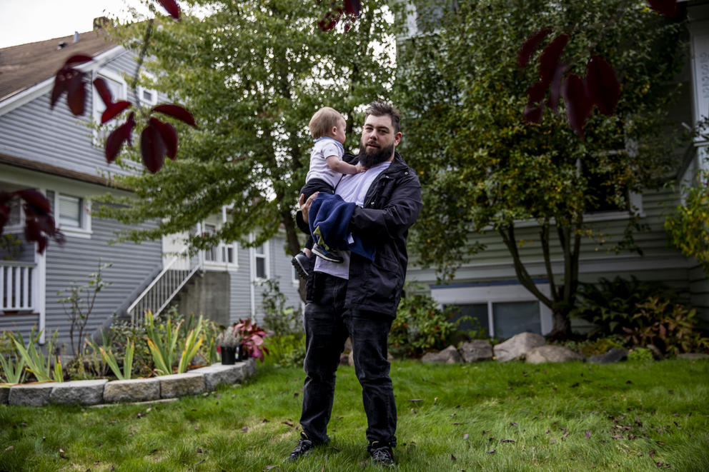 A man holds a young baby in his arms in a backyard
