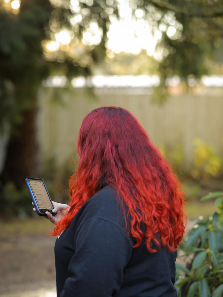A young woman with bright red hair is seen from behind looking at her phone