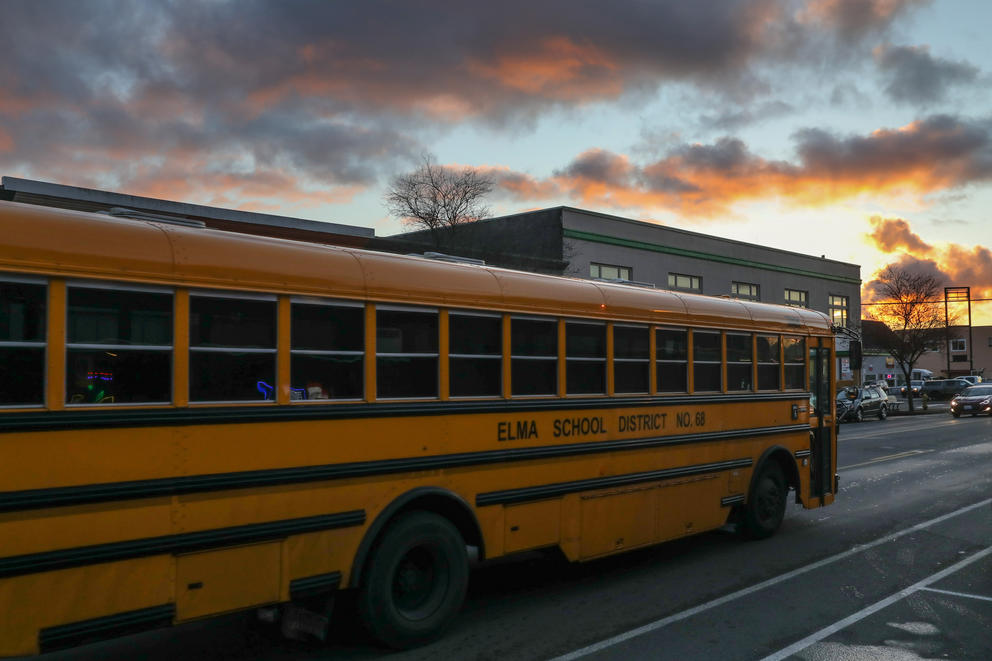 A school bus drives down the street under a sunset colored sky