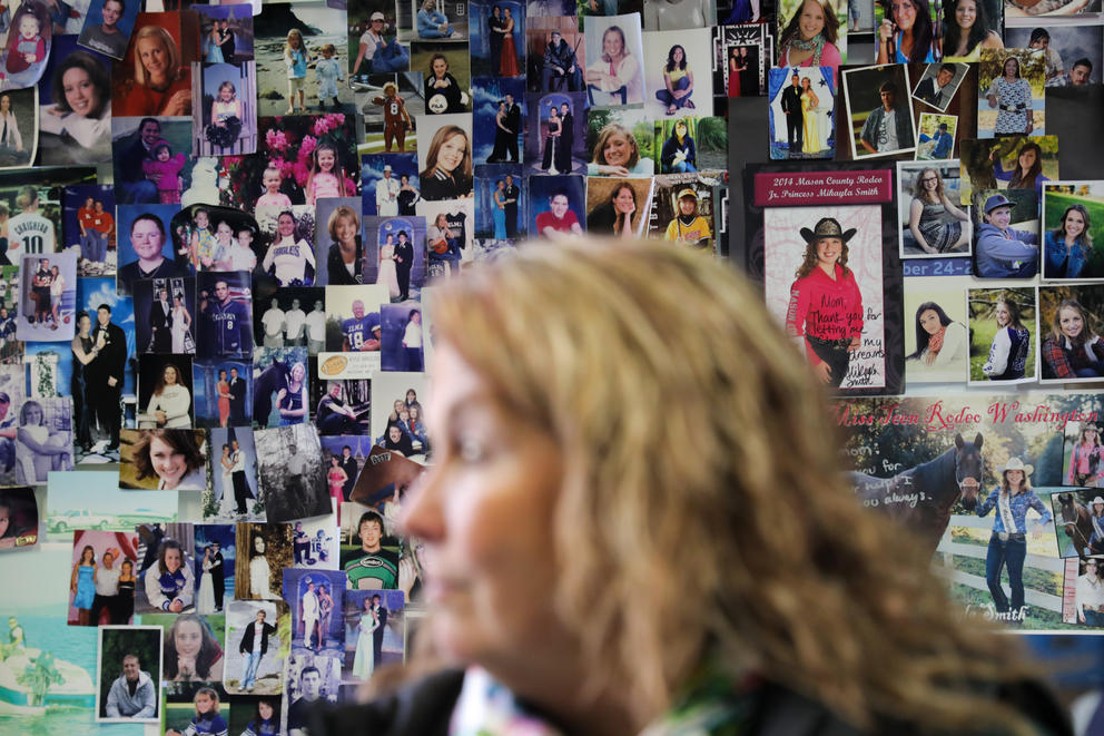 A woman is out of focus in the foreground, behind her a wall of photographs of high school students