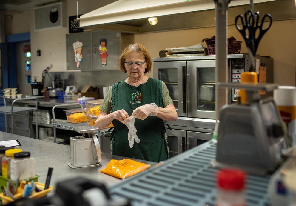 Cathy Rupe stands in a large elementary school kitchen, putting on plastic gloves for food preparation. 