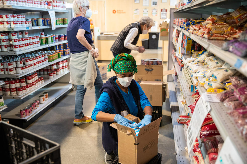 three women stock shelves with food in the aisles of the ballard food bank