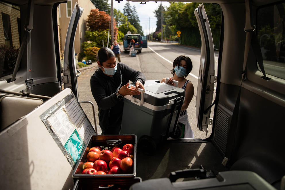 Two food bank workers pack coolers into the back of a van.