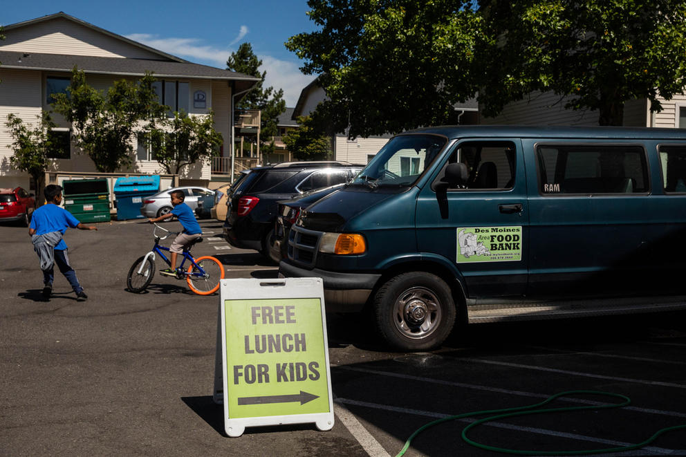 A sign says "FREE LUNCH FOR KIDS" with an arrow to the right pointing at a food bank van.