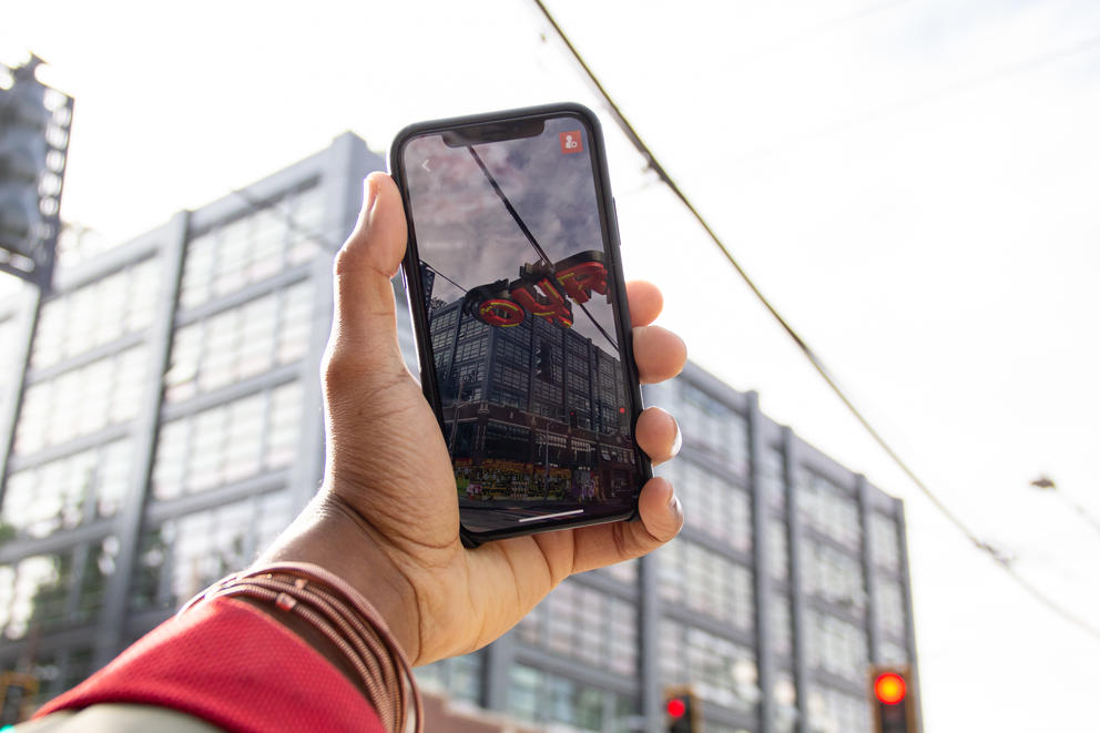 Hand holding a phone featuring an augmented reality artwork in brightred letters on the screen