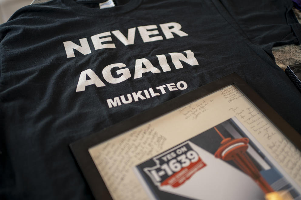 A black shirt with the words "Never again Mukilteo" lays under a picture with writing on the matting. The picture bears the words "Yes on I-1639" and an image of the Space Needle