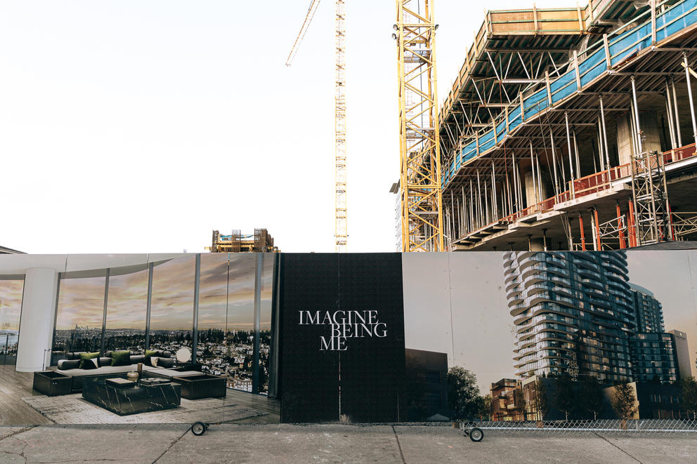 Advertisement wall surrounding an apartment building under construction reads "Imagine being me"