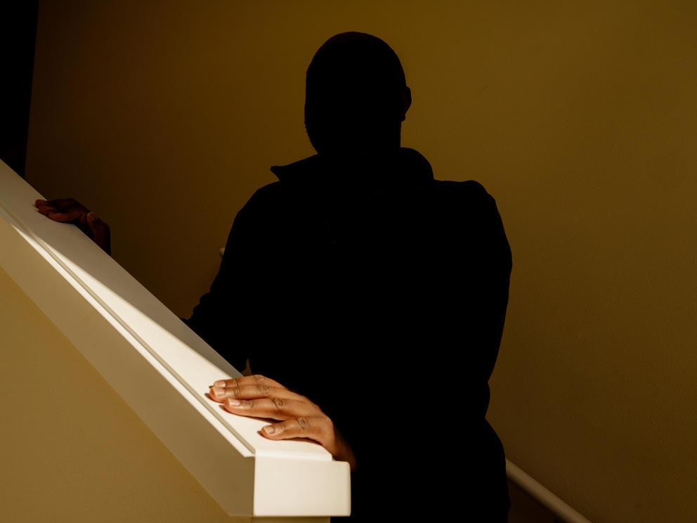 A man in shadow puts his hand on a bannister