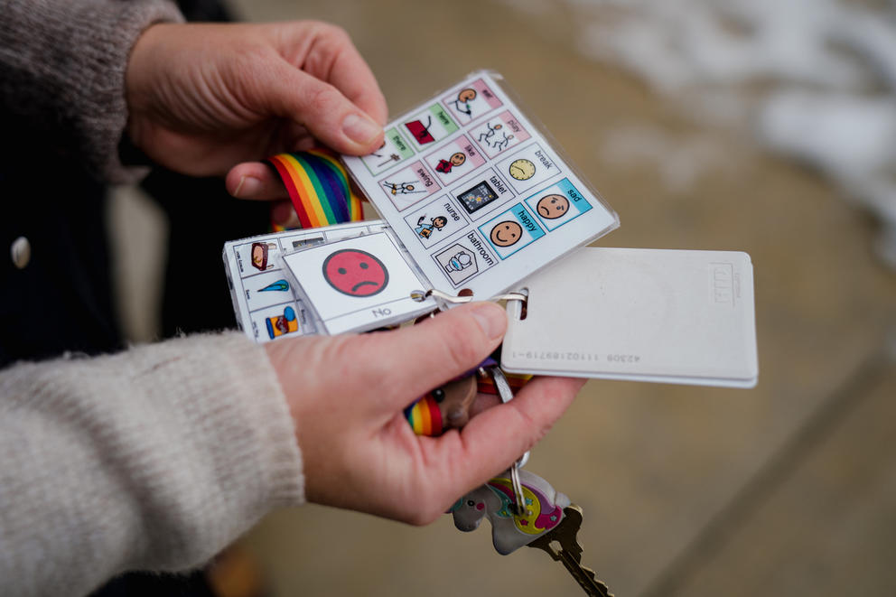 Two hands hold several cards with pictures and words that can help people communicate.