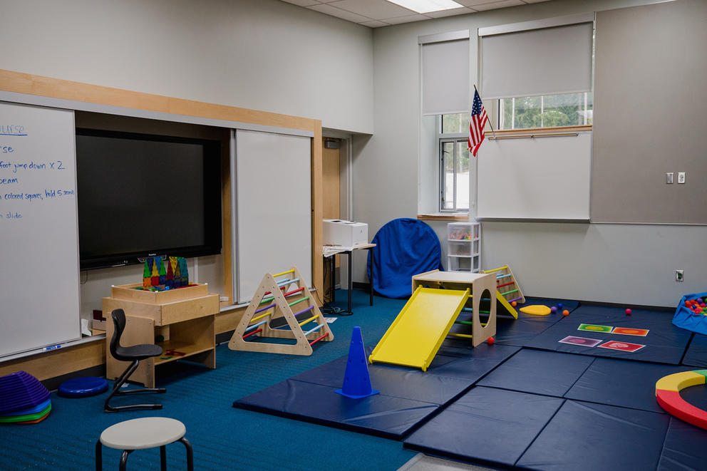 A classroom filled with floor mats, a small slide and other equipment for children to play and practice motor skills.