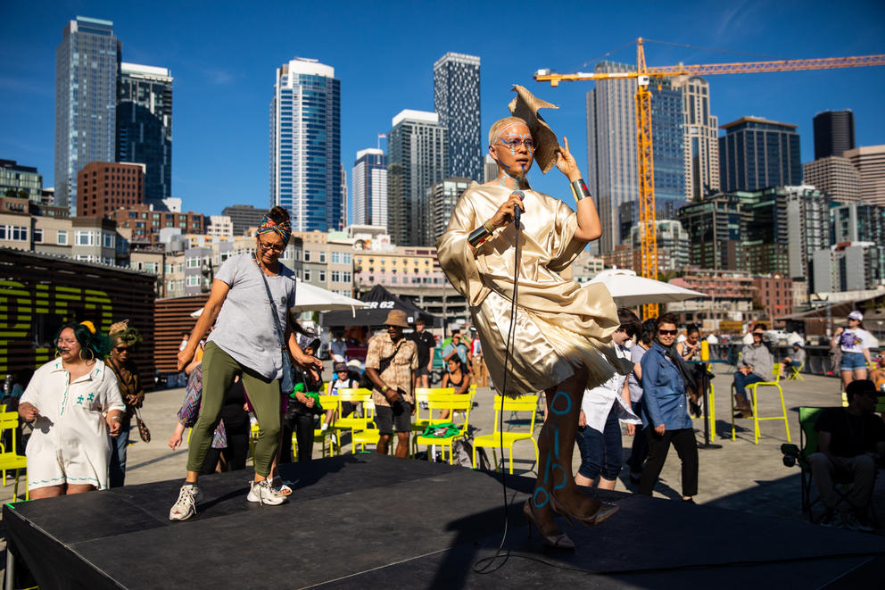 People dance in front of the city of Seattle's skyline, with a crane in the distance