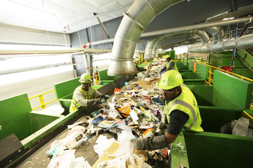 People in safety vests and helmets sort recycling off a conveyer belt