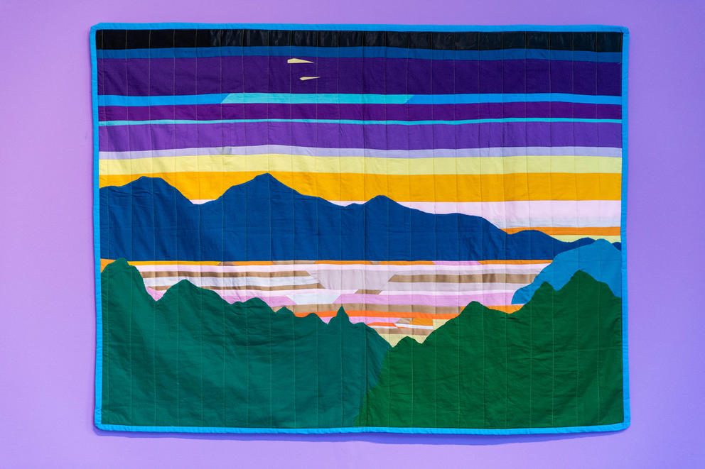 purple wall with a rectangle quilt featuring a Pacific Northwest lake with mountains and trees