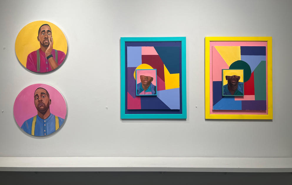 Two round paintings and two vertical paintings of various color blocks hang on a white wall