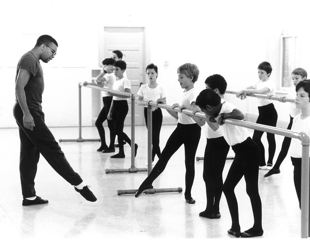 a black and white photo of a man teaching a ballet class full of young boys