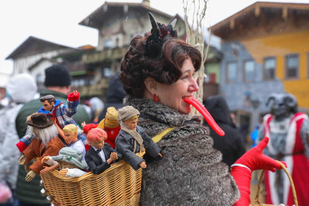 A woman with a basket full of male dolls and a long red tongue walks in a crowd