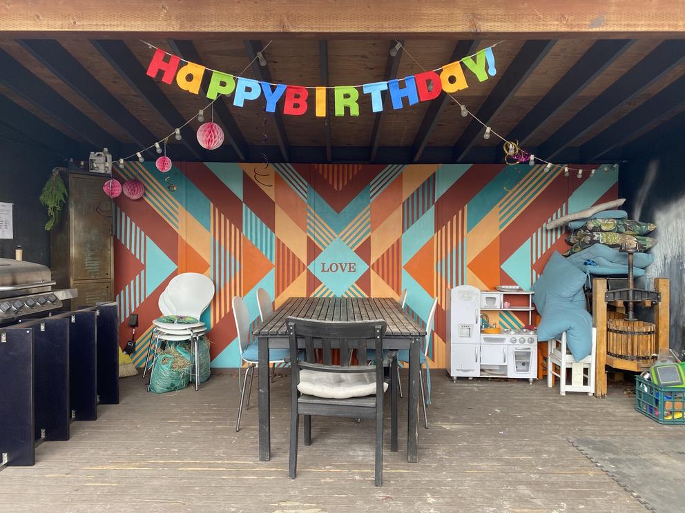 an outdoor dining table with a mural behind it, orange and turquoise stripes pointing to the word love