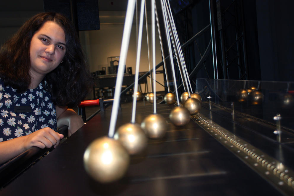 A woman stands next to a pendulum exhibit