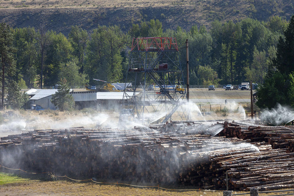 Logs are piled near a tower and helicopter