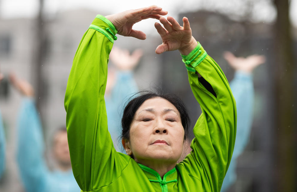 A close up of a woman wearing a green shirt with her arms raised above her head and her eyes closed