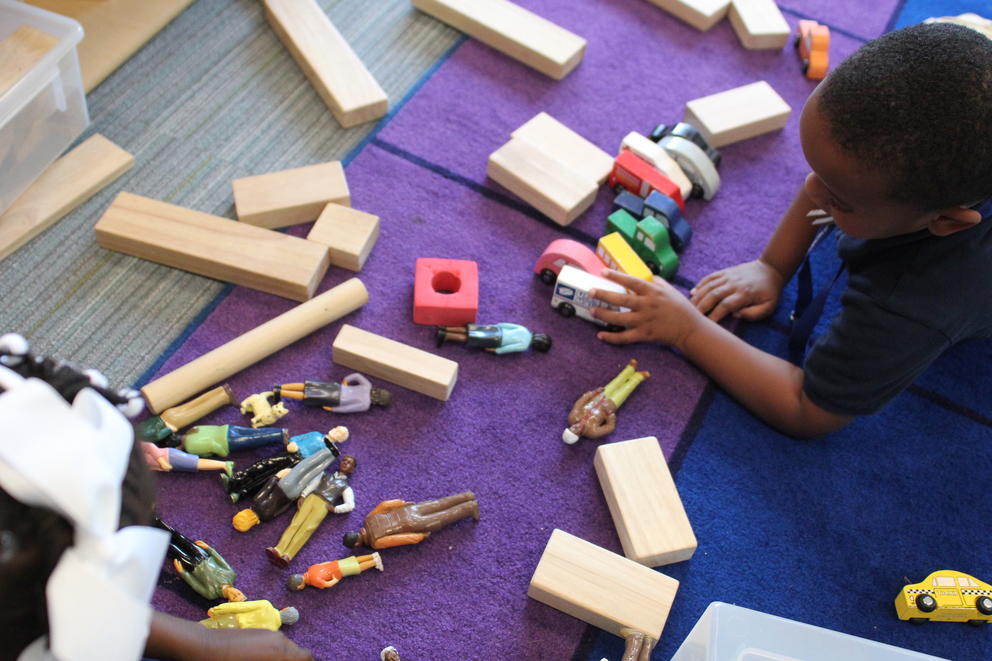 A student sits on a rug playing with blocks