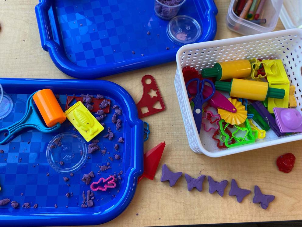 A storage bin of cookie cutters sits next to two trays of colored kinetic sand