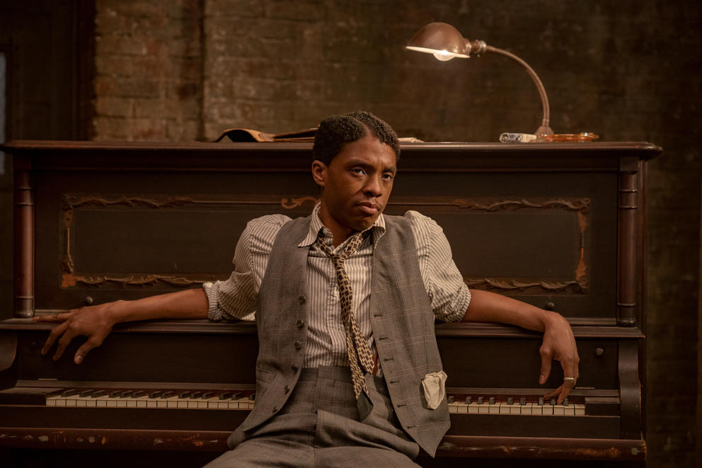 Actor in jazz era clothes sitting in front of piano. 