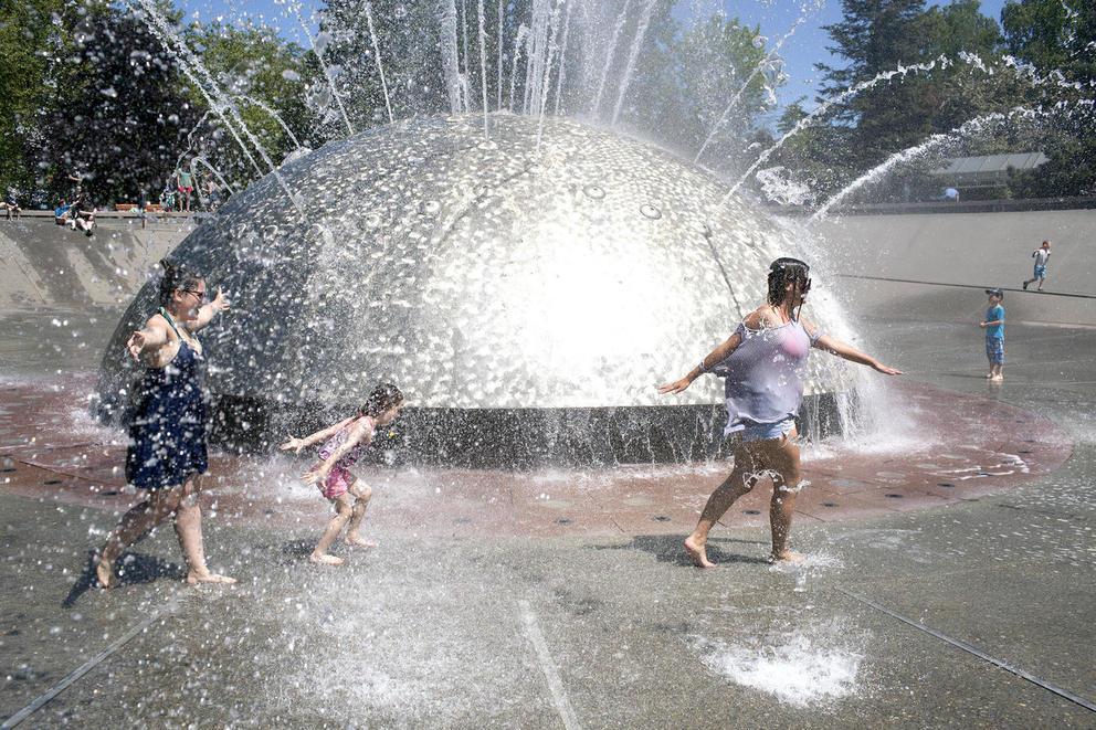 three people run through a fountain as water sprays