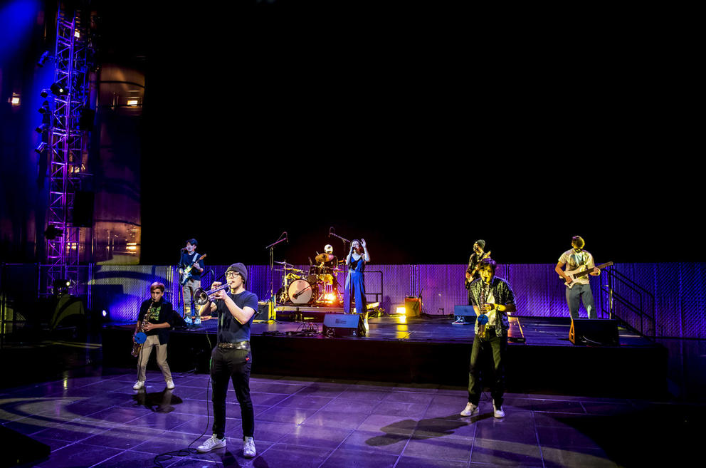 Band on stage and on tile floor in front, purple lighting surrounds them