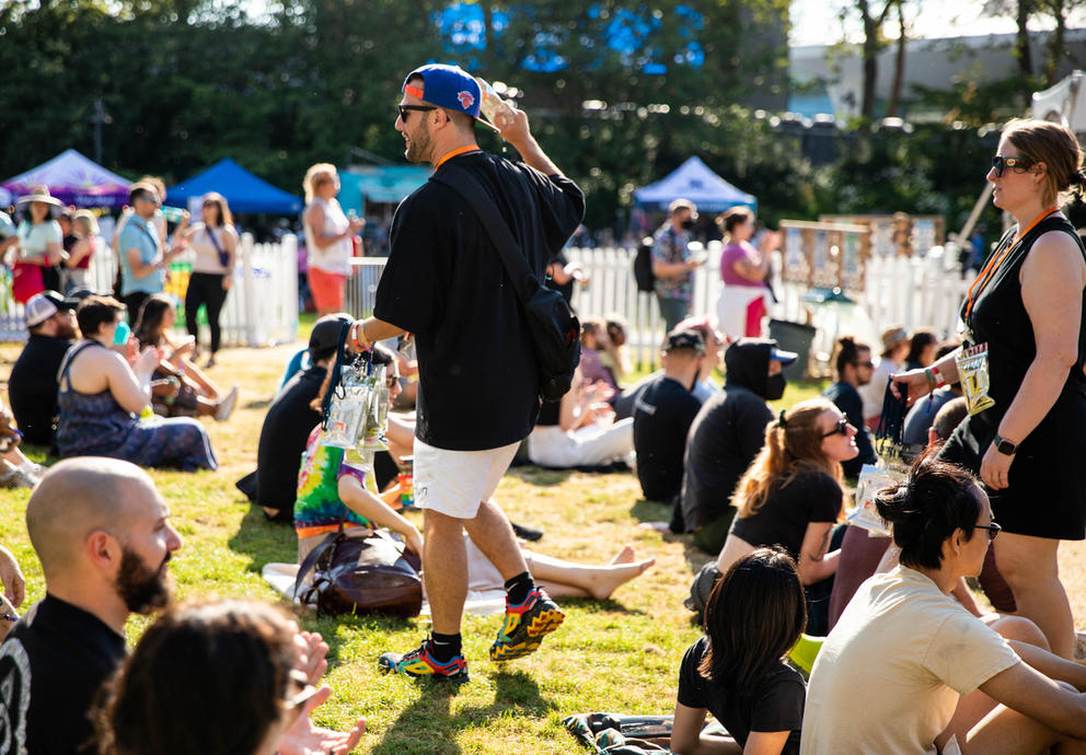Person in black t-shirt and white shors walks through a crowd sitting on a grassy field