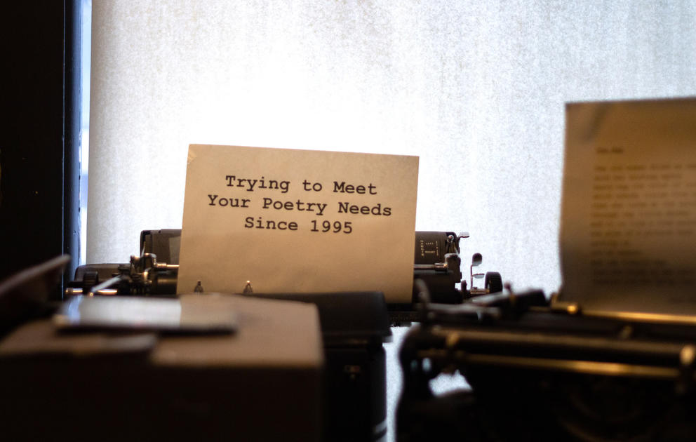 Antique black typewriter with white page and black font, reading:  “Trying to meet your poetry needs since 1995”