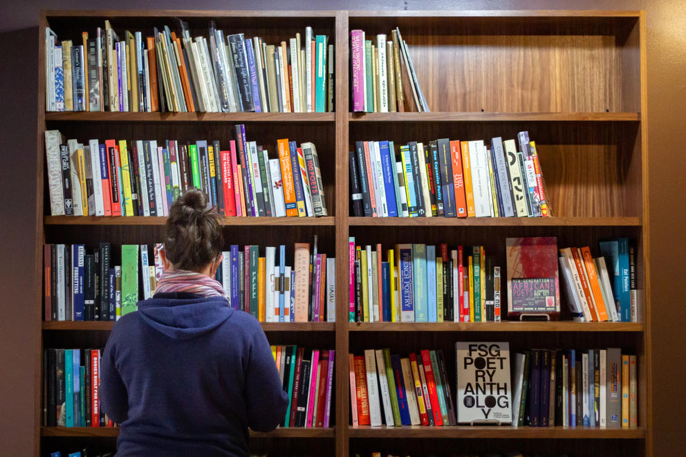 Person in blue sweater stands in front of tall wooden shelves full of books