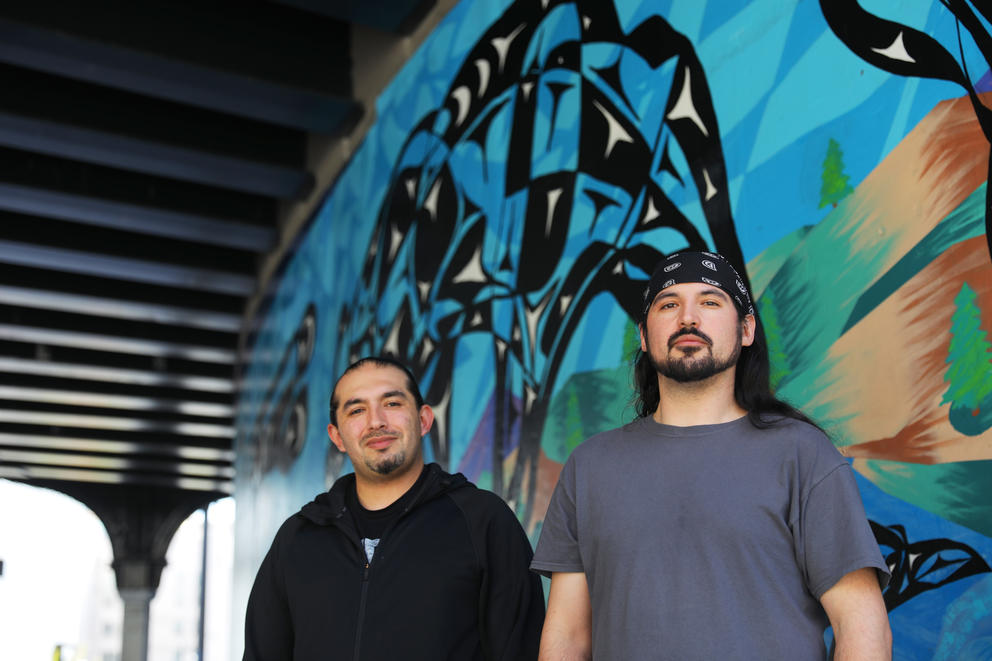 two men pose in front of a mural in seattle