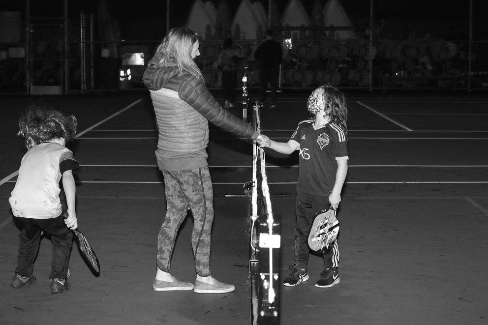 A woman and boy shake hands over a pickleball net. Black and white.